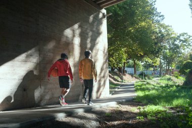 Parkta yürüyen iki kişi, biri basketbol topu taşıyor. Sahne rahat ve rahat, çünkü iki arkadaş birlikte sakin bir yürüyüşün keyfini çıkarıyorlar.