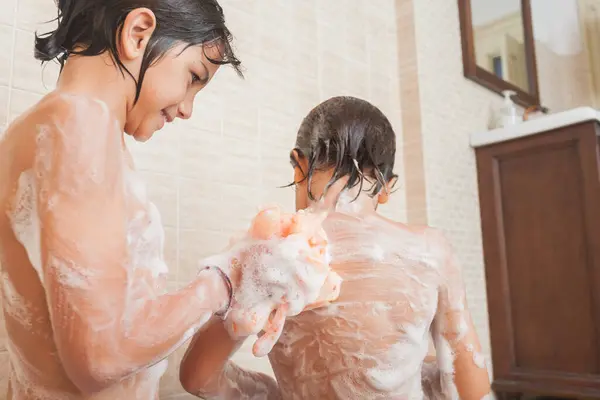 Bir çocuk banyo sırasında küçük kardeşinin sırtını süngerle yıkar. Aile hijyeni ve kişisel bakım