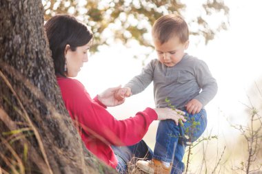 Bir kadın ve bir çocuk bir ağacın gölgesinde oturuyorlar. Kadın çocuğun elini tutuyor.