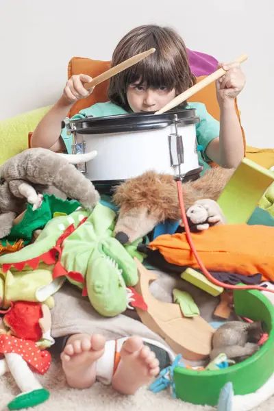Bir çocuk oyuncakların altında gömülüyken davulla oynar. Sahne dağınık ve kaotik, oyuncaklar her yere saçılmış. Çocuk eğleniyor gibi görünüyor..