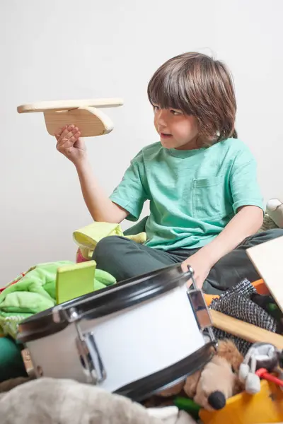 Oyuncak uçak ve oyuncak davul da dahil olmak üzere yerde oyuncaklarla çevrili genç bir çocuk oturuyor. O, uçağı elinde tutuyor ve onunla oyun oynuyor. Çocukluk masumiyeti kavramı