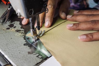 İş yerindeki profesyonel üretim makinesine kumaş dikiyorum. Dikiş işleminin görüntüsünü kapat. Fabrikada terzilik. Bulanık arkaplan.