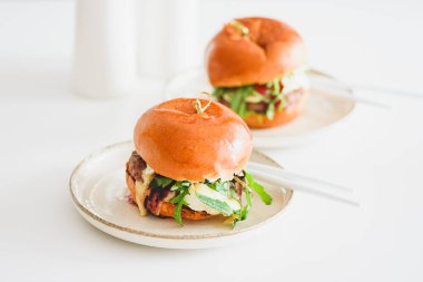 İki lezzetli ev yapımı hamburger, biftek, peynir ve sebzeler beyaz ahşap masada.