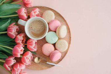 Bir buket pembe lale, bir fincan kahve ve pembe arka planda badem kurabiyesi. Yıldönümü kutlaması. Uzayı kopyala Üst görünüm