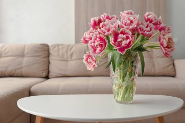 Sehpanın üzerinde pembe laleler ve bej renkli, modern, rahat oturma odasının bulanık arkaplanı. Boşluğu kopyala