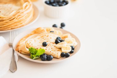 French crepes with banana and blueberries on white table. Copy space