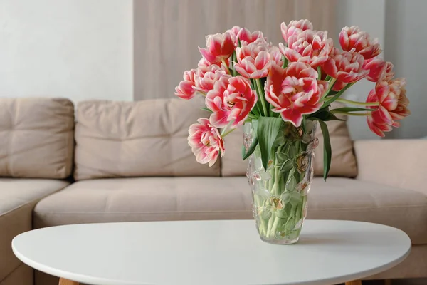 Vase of pink tulips on coffee table with blurred background of beige modern cozy light living room.  Copy space