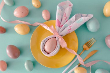 Tabak dekore edilmiş tavşan kulaklı peçete, beyaz laleler ve mavi arka planda Paskalya yumurtaları. Paskalya kutlaması. Düz yatıyordu. Üst görünüm