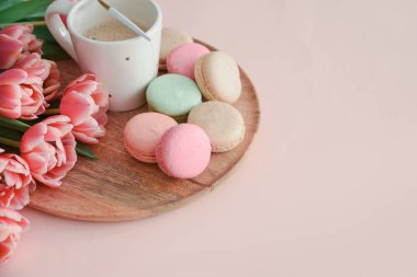 Bir buket pembe lale, bir fincan kahve ve pembe arka planda badem kurabiyesi. Yıldönümü kutlaması. Uzayı kopyala Üst görünüm