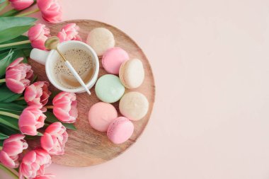 Bir buket pembe lale, bir fincan kahve ve pembe arka planda badem kurabiyesi. Yıldönümü kutlaması. Uzayı kopyala Üst görünüm