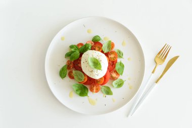 Beyaz ahşap masada domates, kiraz, mozzarella ve fesleğen yapraklı Caprese salatası.