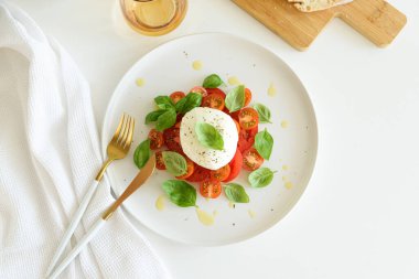 Beyaz ahşap masada domates, kiraz, mozzarella ve fesleğen yapraklı Caprese salatası.