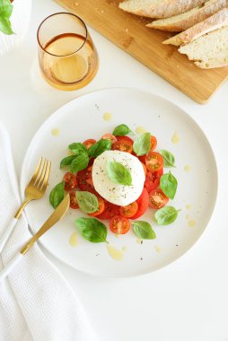 Beyaz ahşap masada domates, kiraz, mozzarella ve fesleğen yapraklı Caprese salatası.