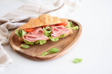Jambonlu ve peynirli kruvasan sandviçi beyaz masada, ahşap tabakta. Sağlıklı kahvaltı..