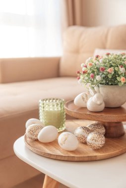 Paskalya yumurtaları, mumlar ve beyaz seramik tavşanlar oturma odasının içindeki ahşap masada.