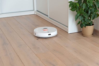 Robot elektrik süpürgesi odayı süpürüyor. Doğal güneşli ışıklar