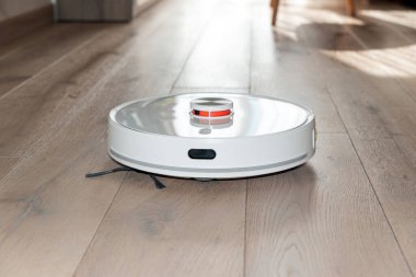 Robot elektrik süpürgesi odayı süpürüyor. Doğal güneşli ışıklar