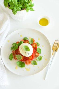 Beyaz ahşap masada domates, kiraz, mozzarella ve fesleğen yapraklı Caprese salatası.