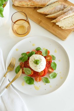 Beyaz ahşap masada domates, kiraz, mozzarella ve fesleğen yapraklı Caprese salatası.