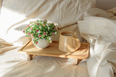 Yatakta kahvaltı: Tahta tepside bir fincan kahve ve buket. Pencere ışığı