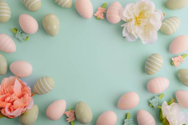 Yeşil arka planda pastel paskalya yumurtaları ve çiçekler. Üst görünüm