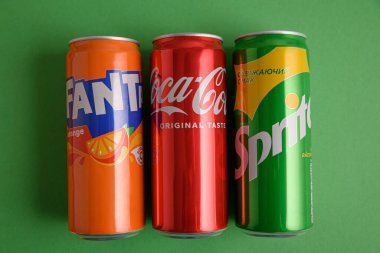 Lviv, Ukrayna - 25 Mart 2025: Yeşil zemin üzerinde demir Coca Cola, Fanta ve Sprite kutuları. Üst görünüm