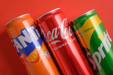 Lviv, Ukrayna - 25 Mart 2025: Kırmızı zemin üzerinde demir Coca Cola, Fanta ve Sprite kutuları. Üst görünüm