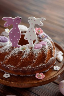 Geleneksel paskalya pastaları, koyu ahşap masa üzerinde tavşan şeklinde zencefilli kurabiyelerle süslenmiş kremalı.