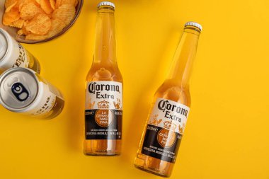 Lviv, Ukrayna - 22 Nisan 2025: Corona Extra bira şişeleri ve sarı arka planda cips kutuları. Üst görünüm