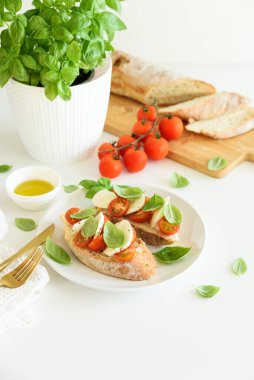 Beyaz ahşap masada mozzarella, kiraz domatesi ve fesleğen yapraklı kızarmış ekmek.