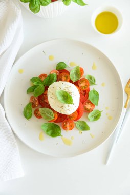 Beyaz ahşap masada domates, kiraz, mozzarella ve fesleğen yapraklı Caprese salatası.
