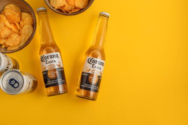 Lviv, Ukrayna - 21 Nisan 2025: Corona Extra bira şişeleri ve sarı arka planda cips kutuları. Üst görünüm