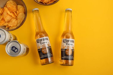 Lviv, Ukrayna - 21 Nisan 2025: Corona Extra bira şişeleri ve sarı arka planda cips kutuları. Üst görünüm