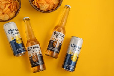 Lviv, Ukrayna - 21 Nisan 2025: Corona Extra bira şişeleri ve sarı arka planda cips kutuları. Üst görünüm