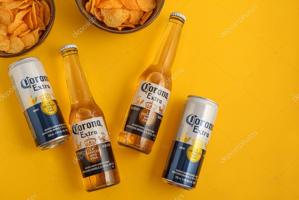 Lviv, Ukraine - April 21, 2025: Corona Extra beer bottles and cans with chips on yellow background. Top view