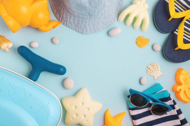 Çocukların plaj çantalarının, kalıpların, hasır şapkaların, sandaletlerin, güneş koruyucu kremlerin ve mavi arka planda güneş gözlüklerinin olduğu çerçevenin çerçevesi. Üst Manzara. Boşluğu kopyala