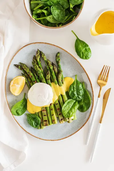 Izgara kuşkonmaz, ıspanak ve beyaz masada Hollandaise sosuyla haşlanmış yumurta. Üst görünüm