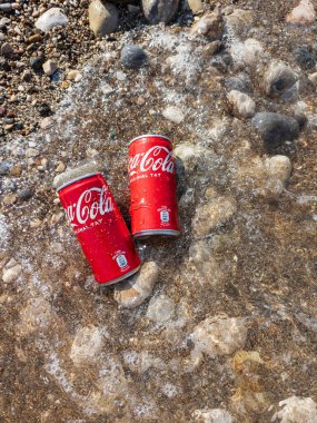 Kemer, Türkiye - Haziran 05, 2025: Okyanus suyu ile kayalık bir sahilde Coca-Cola kutuları. Üst görünüm