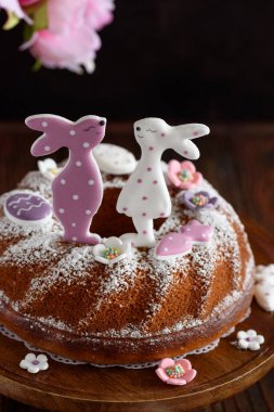 Geleneksel paskalya pastaları, koyu ahşap masa üzerinde tavşan şeklinde zencefilli kurabiyelerle süslenmiş kremalı.