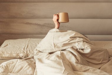 Sıcak bir yataktan kahve fincanı tutan bir el..