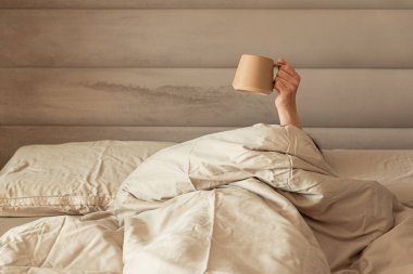 Sıcak bir yataktan kahve fincanı tutan bir el..