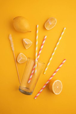 Limonata hazırlıyorum. Limonlar, pipetler ve parlak sarı arka planda bir bardak..