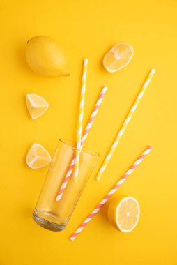 Limonata hazırlıyorum. Limonlar, pipetler ve parlak sarı arka planda bir bardak..