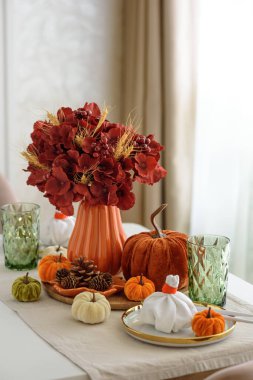 Süslü balkabakları, mumlar ve beyaz ahşap masa üzerindeki iplik ışıkları ile Şükran Günü sofrası.