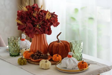 Süslü balkabakları, mumlar ve beyaz ahşap masa üzerindeki iplik ışıkları ile Şükran Günü sofrası.