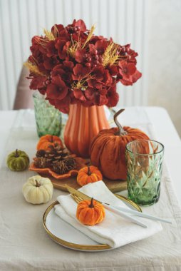 Süslü balkabakları, mumlar ve beyaz ahşap masa üzerindeki iplik ışıkları ile Şükran Günü sofrası.