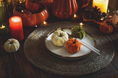 Süslü balkabaklarıyla Şükran Günü sofrası, mumlar ve sicim ışıkları koyu ahşap masa üzerinde.