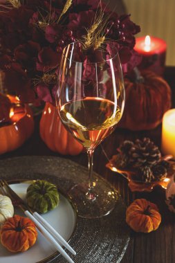 Süslü balkabaklarıyla Şükran Günü sofrası, mumlar ve sicim ışıkları koyu ahşap masa üzerinde.