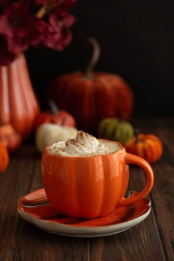 Balkabağı şeklinde bir kupada, sonbahar dekoruyla çevrili, krema ve baharatlı, kabak şeklinde bir latte..