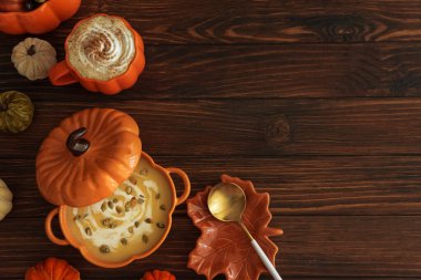 Balkabağı şeklindeki bir kâsede balkabağı çorbası, balkabağı latte, kızarmış ekmek ve koyu ahşap masada şenlikli bir dekor ile sonbahar yemeği. Boşluğu kopyala